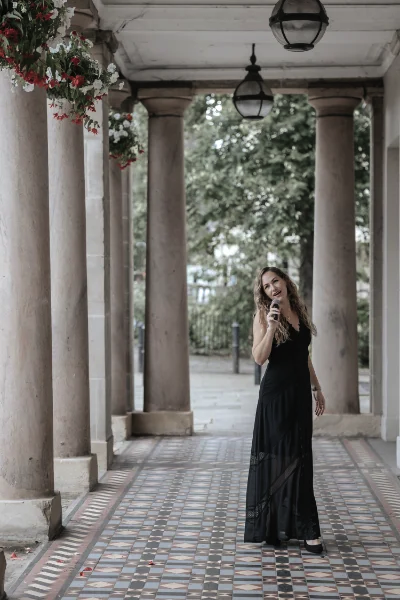 Wedding & event singer Songbird Gebby in dark dress singing with stone columns around