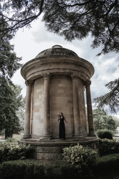Wedding & Event singer Songbird Gebby in dark dress with microphone by stone monument